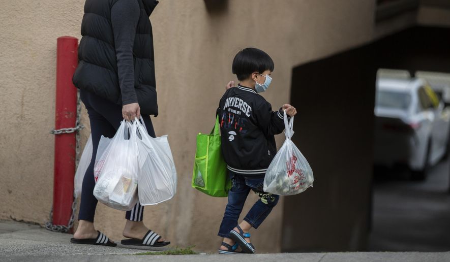 FILE - In this April 2, 2020 file photo, an adult and a child, both wearing face masks amid the coronavirus outbreak, carry bags in the Chinatown neighborhood of Los Angeles. The first U.S. national data on COVID-19 in children suggest that while the virus usually isn’t severe in kids, some do get sick enough to require hospital treatment. The new information is in a federal Centers for Disease Control and Prevention report released Monday, April 6, 2020. (AP Photo/Damian Dovarganes, File)