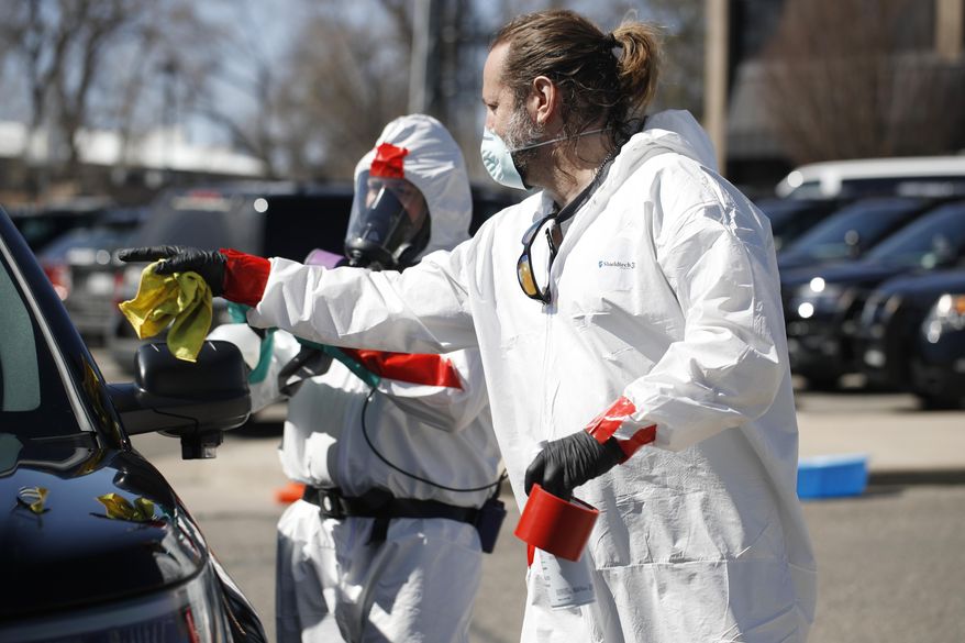 Jason Johnson, front, directs one of the workers from his biohazard cleaning crew as they disinfect a police car, Monday, April 6, 2020, in Wheat Ridge, Colo., to protect officers from the new coronavirus as a statewide stay-at-home order remains in effect in an effort to reduce the spread of the virus. (AP Photo/David Zalubowski)