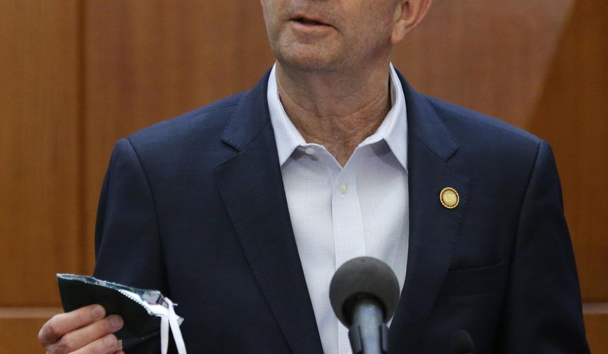 Virginia Gov. Ralph Northam holds up a face mask he carries to help prevent the spread of the coronavirus as he addresses his daily news briefing inside the Patrick Henry Building in Richmond, Va., Monday, April 6, 2020. He said that the mask was made by inmates at one of Virginia's penal facilities. (Bob Brown/Richmond Times-Dispatch via AP)