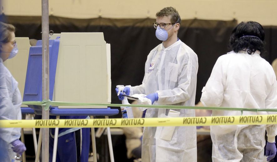 A poll worker sprays down a voting booth after use inside the polling location at Riverside High School  in Milwaukee on Tuesday, April 7, 2020. Voters lined up to cast ballots across Wisconsin on Tuesday, ignoring a stay-at-home order in the midst of the coronavirus pandemic to participate in the state&#x27;s presidential primary election. (Mike De Sisti/Milwaukee Journal-Sentinel via AP)