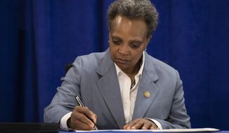 Chicago Mayor Lori Lightfoot signs an executive order to ensure coronavirus-related benefits offered by the city of Chicago are available to immigrants and refugees, Tuesday morning, April 7, 2020. (Ashlee Rezin Garcia/Chicago Sun-Times via AP)