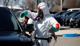 A biohazard cleaner wearing personal protective equipment applies cleaner to a police car, Monday, April 6, 2020, in Wheat Ridge, Colo., as police vehicles are disinfected to protect officers from the new coronavirus as a statewide stay-at-home order remains in effect in an effort to reduce the spread of the virus. (AP Photo/David Zalubowski)