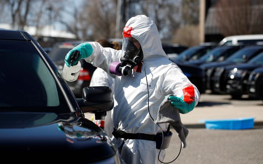 A biohazard cleaner wearing personal protective equipment applies cleaner to a police car, Monday, April 6, 2020, in Wheat Ridge, Colo., as police vehicles are disinfected to protect officers from the new coronavirus as a statewide stay-at-home order remains in effect in an effort to reduce the spread of the virus. (AP Photo/David Zalubowski)