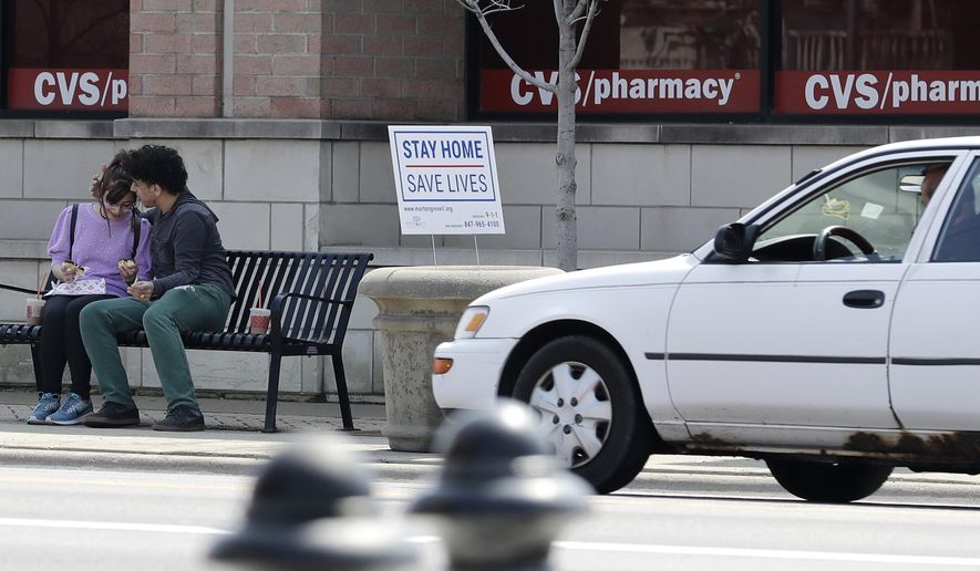 People sit as they chat each other next a "stay home" sign for the coronavirus in Morton Grove, Ill., Tuesday, April 7, 2020. Chicago police to step up social distancing enforcement during warmer weather. (AP Photo/Nam Y. Huh)