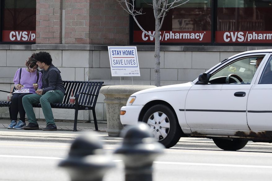 People sit as they chat each other next a "stay home" sign for the coronavirus in Morton Grove, Ill., Tuesday, April 7, 2020. Chicago police to step up social distancing enforcement during warmer weather. (AP Photo/Nam Y. Huh)