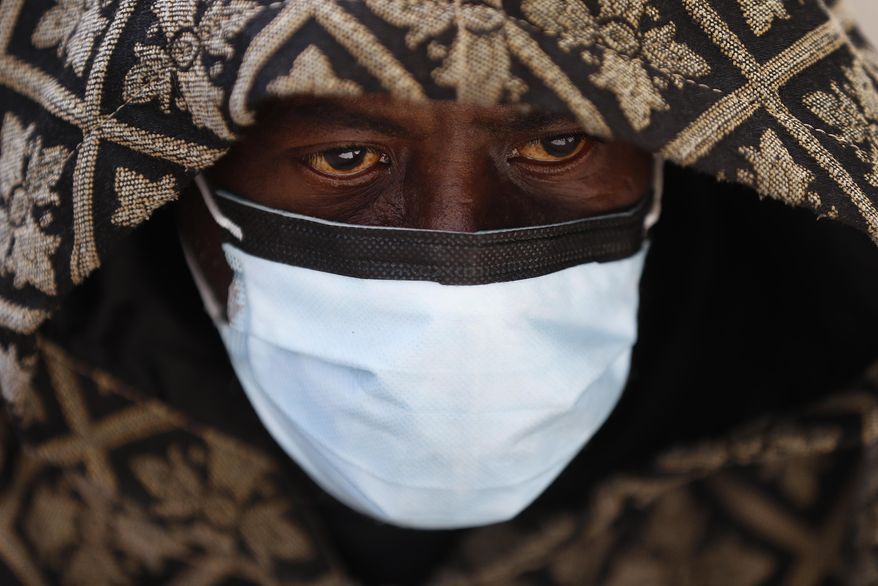 A man wears a protective mask while waiting for a bus in Detroit, Wednesday, April 8, 2020. Detroit buses will have surgical masks available to riders starting Wednesday, a new precaution the city is taking from the new coronavirus COVID-19. (AP Photo/Paul Sancya)