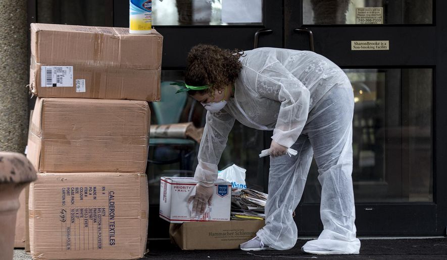 In this Tuesday, March 17, 2020 photo, Elizabeth Johnson disinfects every package that is left outside before bringing it in the SharonBrooke Assisted Living in Newark, Ohio. This is to kill any possible coronavirus that is left on the items. She with other staff members of the senior living residence voluntarily put herself on lockdown, deciding not to leave the building for weeks as a measure to help keep the residents safe. "This is my family too," She said. "Its these people's lives and I'm here to keep them healthy and safe." (Jessica Phelps/The Advocate via AP)
