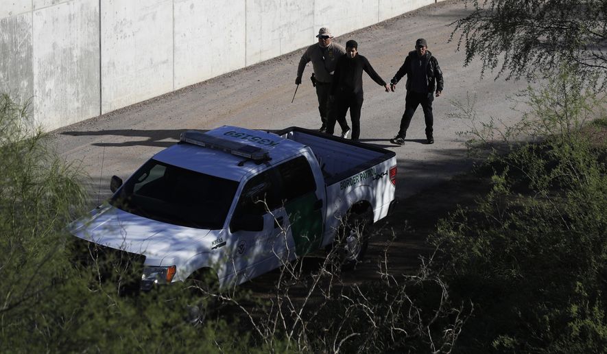 FILE - In this Nov. 16, 2016, file photo, a U.S. Customs and Border Patrol agent walks with suspected immigrants caught entering the country illegally along the Rio Grande in Hidalgo, Texas. The Trump administration has quietly shut down the nation's asylum system for the first time in decades amid coronavirus concerns, largely because holding people in custody is considered too dangerous. (AP Photo/Eric Gay, File)