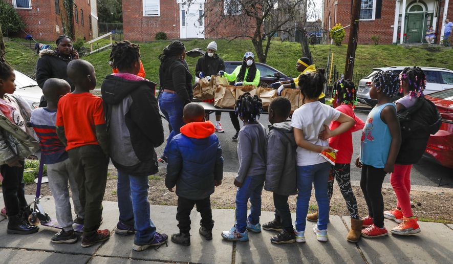 In this March 29, 2020, photo, volunteers India Blocker-Ford, center, D.J. Wood, left, and Regina Summers, right, sort donated bags of hot meals while children wait for the food to be distributed in southeast Washington. Neighborhood deliveries are part of a new Martha's Table initiative, along with community partners, to get needed food directly to the neighborhoods they serve. Local volunteers are the tip of the spear for a grassroots community effort to keep Washington's poorest neighborhoods fed during the unprecedented coronavirus crisis which has nearly shut down the American economy. (AP Photo/Jacquelyn Martin)