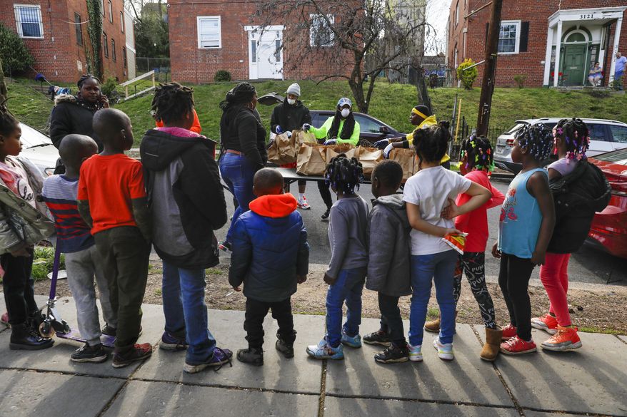 In this March 29, 2020, photo, volunteers India Blocker-Ford, center, D.J. Wood, left, and Regina Summers, right, sort donated bags of hot meals while children wait for the food to be distributed in southeast Washington. Neighborhood deliveries are part of a new Martha's Table initiative, along with community partners, to get needed food directly to the neighborhoods they serve. Local volunteers are the tip of the spear for a grassroots community effort to keep Washington's poorest neighborhoods fed during the unprecedented coronavirus crisis which has nearly shut down the American economy. (AP Photo/Jacquelyn Martin)