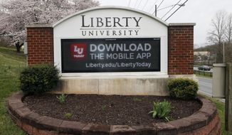 In this March 24 , 2020, file photo, a sign marks the entrance to Liberty University in Lynchburg, Va. The university, led by Jerry Falwell Jr., is pushing for criminal trespassing charges to be lodged against two journalists who pursued stories about why the evangelical college has remained partially open during the coronavirus outbreak. (AP Photo/Steve Helber) ** FILE **