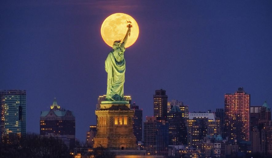 In this March 9, 2020, photo, the full moon rises behind the Statue of Liberty in New York. From California to Colorado to Georgia and New York, Americans are taking a moment each night at 8 to howl to thank the nation&#39;s health care workers and first responders for their selfless sacrifices during the coronavirus pandemic. (AP Photo/J. David Ake, File)