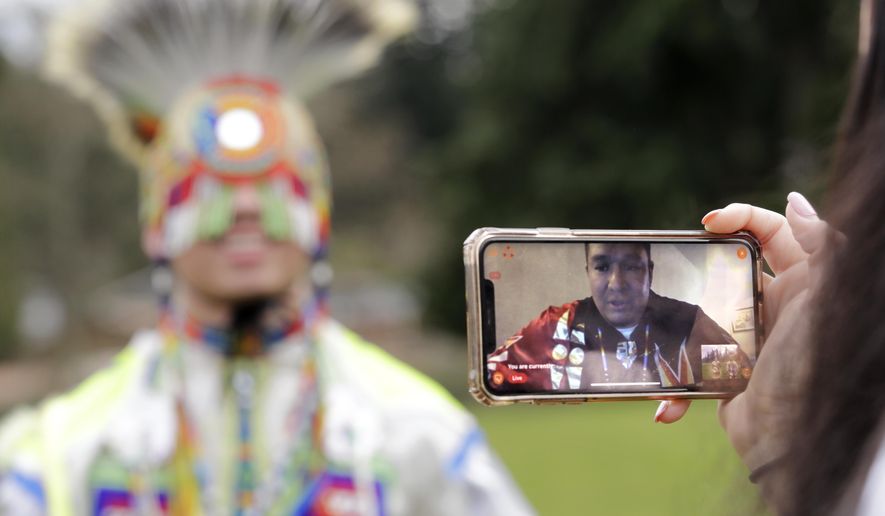 In this photo taken Saturday, April 4, 2020, moderator Whitney Rencountre, a Crow Creek Dakota tribal member, is seen on a screen from Rapid City, S.D., as he talks with Wakiyan Cuny, a Dakota and Lakota tribal member, during a live streamed powwow, in Puyallup, Wash. The largest powwows in the country have been canceled or postponed amid the spread of the coronavirus. Tribal members have found a new outlet online with the Social Distance Powwow. They're sharing videos of colorful displays of culture and tradition that are at their essence meant to uplift people during difficult times. (AP Photo/Elaine Thompson)