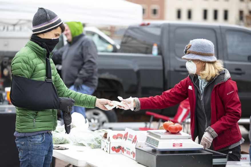 A vendor sells fresh produce as the Carmel Farmers Market opened in Carmel, Ind., Saturday, April 11, 2020. The market practiced social distancing and increased distances between vendors to slow the spread of the coronavirus as the vendors sold their fresh produce, meats and and prepared foods. (AP Photo/Michael Conroy)