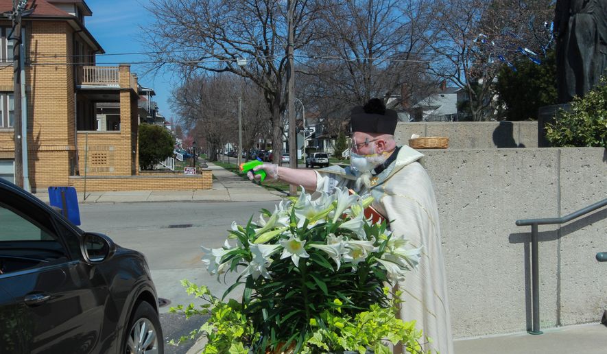 The Rev. Timothy Pelc blesses Easter baskets on Saturday, April 11, 2020, outside St. Ambrose Church in Grosse Pointe Park, Mich. Pelc, wearing church vestments and protective gear against the coronavirus, offered a prayer and sprayed holy water from a squirt gun instead of blessing baskets inside the church during the coronavirus outbreak. (Natalie White via AP)