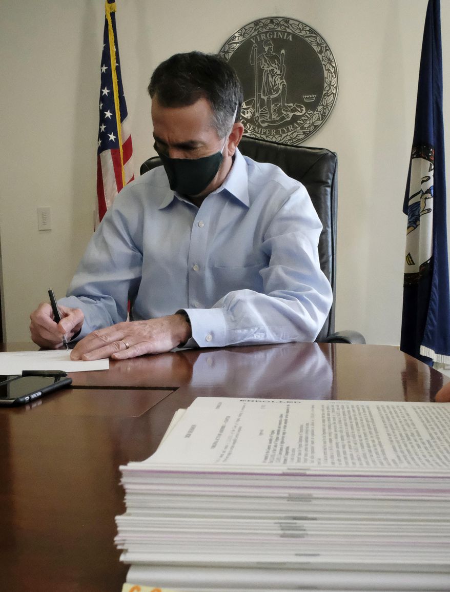 Virginia Governor Ralph Northam wears a mask as signs a piece of legislation from the stack, foreground, in his conference room inside the Patrick Henry Building in Richmond, Va., Friday, April 10, 2020. Northam has a midnight Saturday, April 11, deadline to either sign, amend or veto all legislation passed by the General Assembly. Northam and staff assistants in the room wore masks as a precaution against COVID-19. (Bob Brown/Richmond Times-Dispatch via AP)