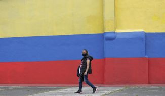 A woman wearing a protective face mask walks next to a house painted with colors of Colombia&#39;s flag, during the lockdown ordered by the government in an effort to prevent the spread of the new coronavirus, in Bogota, Colombia, Tuesday, April 14, 2020. (AP Photo/Fernando Vergara)