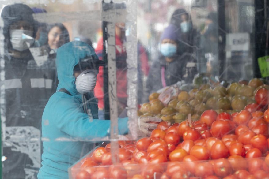 A woman wears a mask to protect against the coronavirus as she shops for produce at a fruit and vegetable stand, Tuesday, April 14, 2020, in Corona neighborhood of the Queens borough of New York. (AP Photo/Mary Altaffer)