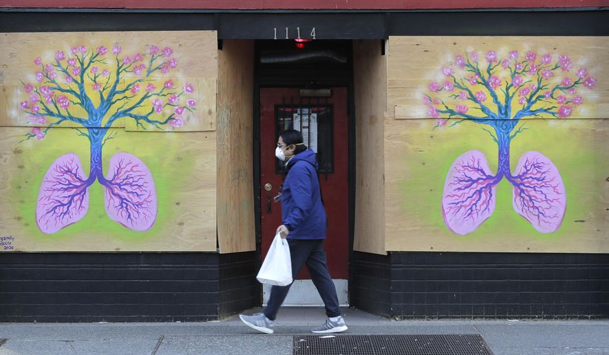 A pedestrian wearing a mask walks past paintings featuring lungs and a tree by Burgandy Viscosi on the boarded-up Re-Bar nightclub and theatre, Tuesday, April 14, 2020, in downtown Seattle. Streets and sidewalks in the area were quiet Tuesday as most people in the city are staying and working at home due to the outbreak of the coronavirus. (AP Photo/Ted S. Warren)