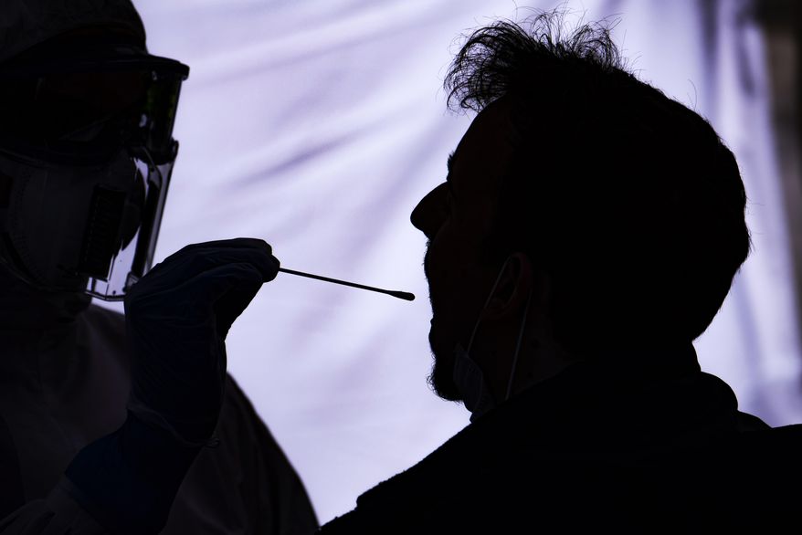 A helper of the German Red Cross DRK in protective suit, left, takes a smear from a patient outside a car, right, during the official opening of a drive-through (drive-in) COVID-19 testing center at the fair ground in Dresden, eastern Germany, Wednesday, April 15, 2020. Germany leads the world in recoveries from COVID-19 infection, according to numbers from Johns Hopkins University. (AP Photo/Jens Meyer)