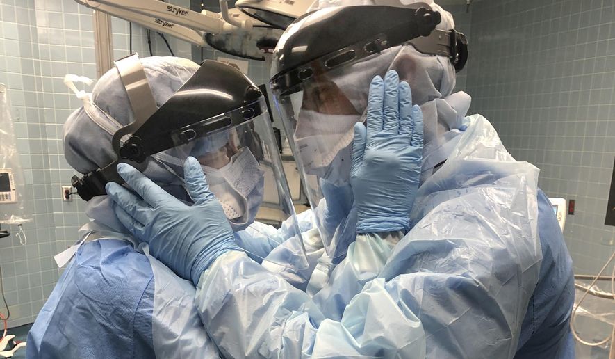 In this March 30, 2020 photo provided by Chief Nurse Anesthetist Nicole Hubbard, nurses Mindy Brock and Ben Cayer, wearing protective equipment, hold each other and look into each other's eyes, in Tampa General Hospital in Tampa, Fla. “Everybody’s talking about the photo,” says Cayer, 46. It strikes a chord “because we’re all going through the same thing right now and it’s a symbol of hope and love.” Brock, 38, adds: “What’s important is that we stick together, we work together, and we always support each other. And not just Ben and I, but the human race right now.” (Nicole Hubbard via AP)