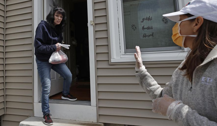 In this April 15, 2020 photo, Neighbors in Need volunteer Julie Prentiss, right, delivers groceries to a client, Wendy, in Lawrence, Mass. During the coronavirus pandemic, NIN is providing food for about 600 families each week. (AP Photo/Elise Amendola)