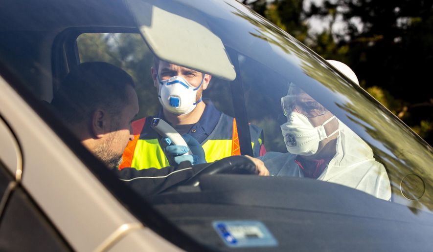 The temperature of a driver arriving from Slovenia is checked by a Hungarian health worker as a precautionary measure against the spreading of coronavirus in a parking place of M70 motorway near Csornyefold, Hungary, Thursday, March 12, 2020. The Hungarian government announced the state of emergency on Wednesday, re-establishing controls along the Austrian and Slovenian borders and prohibiting entry into Hungary for foreign nationals arriving from Italy, China, South Korea and Iran. For most people, the new coronavirus causes only mild or moderate symptoms, such as fever and cough. For some, especially older adults and people with existing health problems, it can cause more severe illness, including pneumonia.  (Gyorgy Varga/MTI via AP)