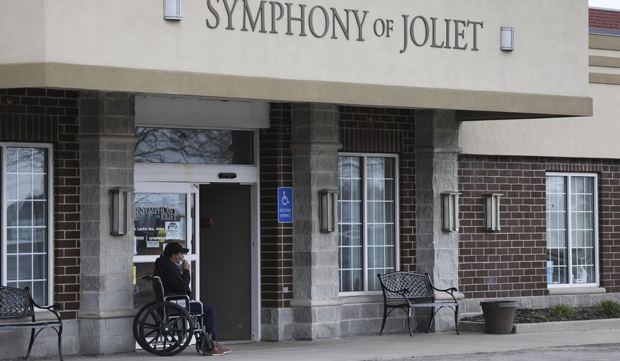 This Wednesday, April 15, 2020 photo shows a man sitting outside the main doors of Symphony Nursing home in Joliet, Ill.  A spokeswoman for the nursing home in the northern Illinois community says several residents and a staff member at the facility have died of the coronavirus. (Abel Uribe/Chicago Tribune via AP)