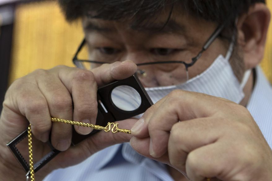 A Thai shopkeeper checks a gold necklace after a customer sold the piece to the gold shop in Bangkok, Thailand, Thursday, April 16, 2020. With gold prices rising to a seven-year high, many Thais have been flocking to gold shops to trade in their necklaces, bracelets, rings and gold bars for cash, eager to earn profits during an economic downturn.(AP Photo/Sakchai Lalit)