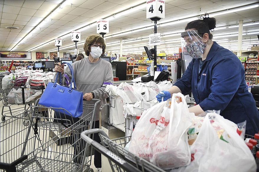 Delores Browning, lefdt, waits for Molly Stanley to bag her groceries at Goodson's Supermarket in Oceana, W.Va. Wednesday, April 8, 2020. On Tuesday, the health department reduced the number shoppers to only 10 at a time. Goodson's supplied their employees each with face masks and most chose to wear them and they also offered to shop for their customers avoiding long wait times to enter the store. (Rick Barbero/The Register-Herald via AP)