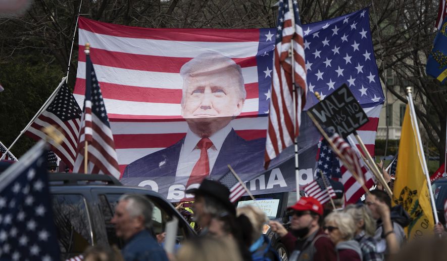 A banner of President Trump on an American flag is held above a crowd demanding the state's Stay at Home order be lifted during a "Liberate Minnesota" protest in St. Paul, Minn., on Friday, April 17, 2020. A growing number of protests are being staged across the U.S. to oppose stay-at-home orders amid the coronavirus pandemic. (Evan Frost/Minnesota Public Radio via AP)