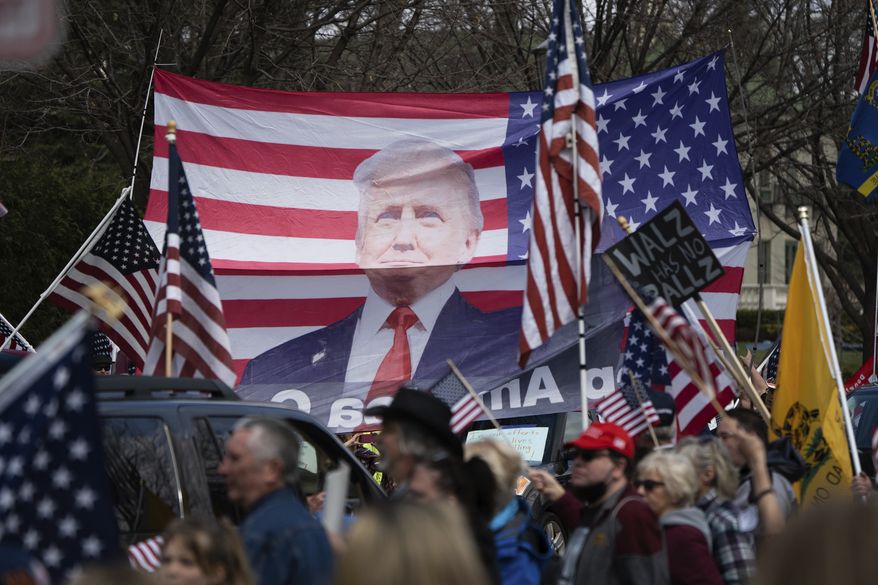 A banner of President Trump on an American flag is held above a crowd demanding the state's Stay at Home order be lifted during a "Liberate Minnesota" protest in St. Paul, Minn., on Friday, April 17, 2020. A growing number of protests are being staged across the U.S. to oppose stay-at-home orders amid the coronavirus pandemic. (Evan Frost/Minnesota Public Radio via AP)