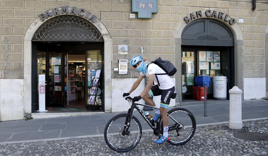In this image taken on Tuesday, April 14, 2020, Italian professional cyclist Davide Martinelli, rides his bike after collecting medicine at a pharmacy to be delivered to residents in Rovato, near Brescia, Northern Italy. There are no fans lining the road. No teammates providing support. And no race to win. Professional cyclist Davide Martinelli has achieved a moral victory, though, by using his bike to help deliver medicine to elderly residents of his hometown in northern Italy during the coronavirus pandemic. (AP Photo/Luca Bruno)