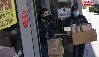 In this April 15, 2020, photo, employees, wearing protective gloves and masks, walk to-go orders to waiting cars at Founding Farmers restaurant in Potomac, Md. Founding Farmers is closed to in-restaurant dining during the coronavirus outbreak but they are providing delivery, and curbside pick-up to-go, for meals and groceries. (AP Photo/Carolyn Kaster)