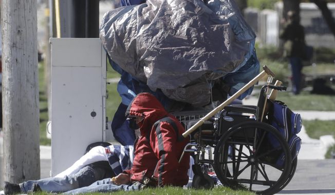 A man sits near a sidewalk Tuesday, April 14, 2020, in Salt Lake City. Salt Lake City is leasing a hotel to shelter homeless people over 60 with underlying health conditions who are particularly vulnerable to coronavirus infections. People began checking into the 130-bed hotel Friday and can stay for at least two weeks with a possible extension, said county Mayor Jenny Wilson. Salt Lake City has confirmed a handful of cases in the homeless community, where preventative steps such as hand-washing and social distancing are more difficult. (AP Photo/Rick Bowmer)