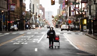 In this April 13, 2020, file photo a person wearing a protective mask walks down Market Street in Philadelphia. Across an arc of vital swing states, the coronavirus has put politics on an uneasy pause. Political fights are raging among state leaders from Iowa to Pennsylvania over the handling of the pandemics impact. (AP Photo/Matt Rourke, File)