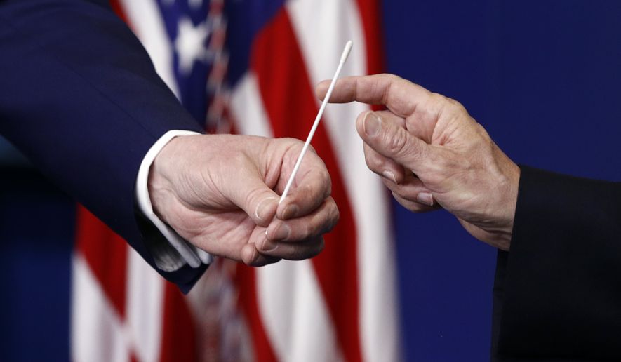 President Donald Trump, left, hands a swab that could be used in coronavirus testing to Vice President Mike Pence during a coronavirus task force briefing at the White House, Sunday, April 19, 2020, in Washington. (AP Photo/Patrick Semansky)