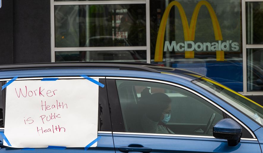 CORRECTS DATE - A protester stops momentarily at a McDonald's drive-thru, as she joins fast-food workers protesting for a second day, outside the restaurant in the Crenshaw district of Los Angeles, Monday, April 6, 2020. The protesters were demanding guaranteed paid sick leave for all workers during the coronavirus outbreak, as well as personal protection equipment, after a co-worker became sick with the virus. (AP Photo/Damian Dovarganes)