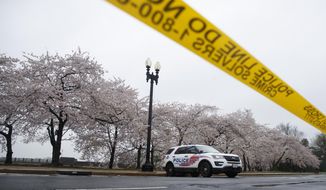In this March 23, 2020, file photo a Washington, D.C. Metropolitan Police vehicle is parked on the other side of a tape police line along the Tidal Basin as cherry blossoms cover the trees, in Washington. The nation&#39;s capital, like most of the nation itself, is largely shuttered. (AP Photo/Carolyn Kaster, File)