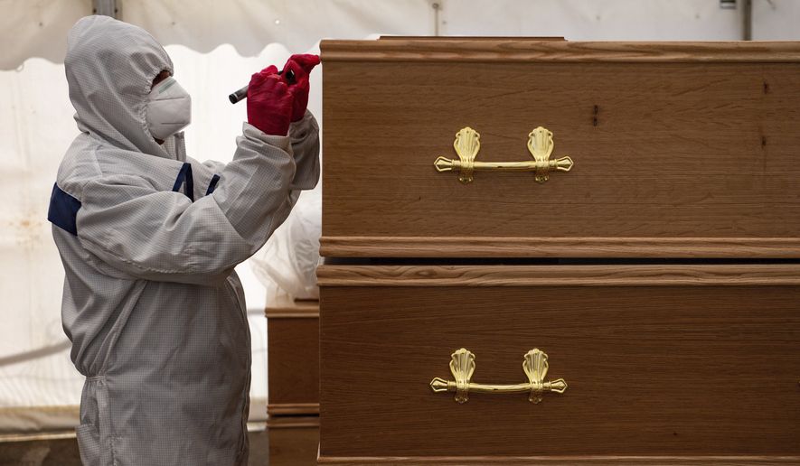 A volunteer marks coffins at Central Jamia Mosque Ghamkol Sharif in Birmingham, England which is operating a temporary morgue during the COVID-19 pandemic Monday, April 20, 2020. The mosque already runs one of the city&#39;s oldest Muslim funeral services and is accepting deceased of all faiths in separate coronavirus and non-coronavirus facilities. (Jacob King/PA via AP)