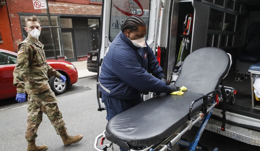 FILE - In this April 17, 2020, file photo, an emergency medical worker cleans his gurney at his ambulance as a member of the National Guard arrives outside Cobble Hill Health Center in the Brooklyn borough of New York. The CEO of the nursing home says his facility quickly became overwhelmed after nearly a third of the staff went out sick and those left began wearing garbage bags because of a shortage of protective gear. (AP Photo/John Minchillo, File)