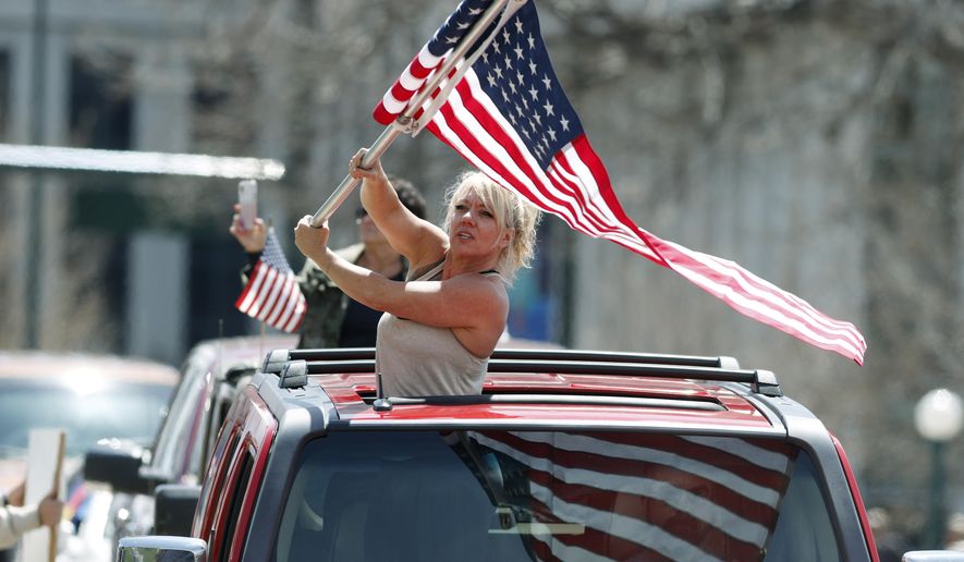 A protester waves an American flag during a car protest against the stay-at-home order issued by Colorado Governor Jared Polis to stem the spread of the new coronavirus Sunday, April 19, 2020, in Denver. (AP Photo/David Zalubowski)