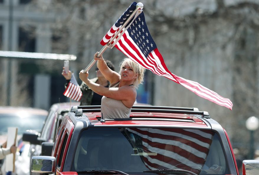 A protester waves an American flag during a car protest against the stay-at-home order issued by Colorado Governor Jared Polis to stem the spread of the new coronavirus Sunday, April 19, 2020, in Denver. (AP Photo/David Zalubowski)