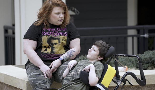 In this Thursday, April 2, 2020 photo, Anna Hauser sits with her son Xavier, 14 in the courtyard of their Madison, Wis., apartment complex.  (Steve Apps/Wisconsin State Journal via AP)
