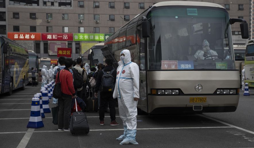 A worker in protective clothing waits to guide passengers from Wuhan to board buses after they arrive on a high speed train in Beijing on Sunday, April 19, 2020. Wuhan, the city at the center of the global coronavirus epidemic, lifted a 76-day lockdown early April and allowed people to leave for destinations across China. (AP Photo/Ng Han Guan)