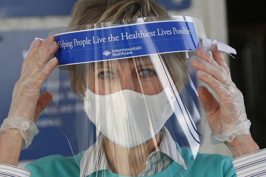 In this Saturday, April 18, 2020, photo, Jean Bingham, President of the Relief Society, adjust her afce shield during a mask drop off in Murray, Utah. The mask was sewn as part of a project in Utah organized by The Church of Jesus Christ of Latter-day Saints and several health care organizations that has called on thousands of residents to try and make five million medical-grade masks for health care workers. The church's women's organization, called the Relief Society, has tapped into its network of thousands of volunteers from around the world for help. (AP Photo/Rick Bowmer)