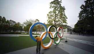 A child plays at the Olympic rings in front of the New National Stadium in Tokyo Tuesday, April 21, 2020. An open conflict broke out Tuesday between Tokyo Olympic organizers and the IOC over how much to divulge about who will pay for the unprecedented year-long postponement. (AP Photo/Eugene Hoshiko)