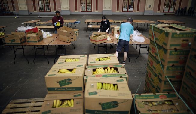 Volunteers for the Edible London food project remove the plastic packaging and check the quality of donated bananas to be put in food packs and delivered to residents who need it in the Haringey Council area, at a hub setup as a result of coronavirus inside the Alexandra Palace venue, in north London, Tuesday, April 21, 2020. The highly contagious COVID-19 coronavirus has impacted on nations around the globe, many imposing self isolation and exercising social distancing when people move from their homes. (AP Photo/Matt Dunham)