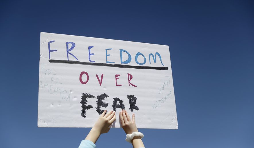 FILE - In this April 21, 2020, file photo a person holds a sign while gathering with others to protest stay-at-home orders put into place due to the COVID-19 outbreak outside the Missouri Capitol in Jefferson City, Mo. Amid pockets of attention-grabbing protests, a new survey finds Americans remain overwhelming in favor of stay-at-home orders and other efforts to slow the spread of coronavirus. (AP Photo/Jeff Roberson, File)