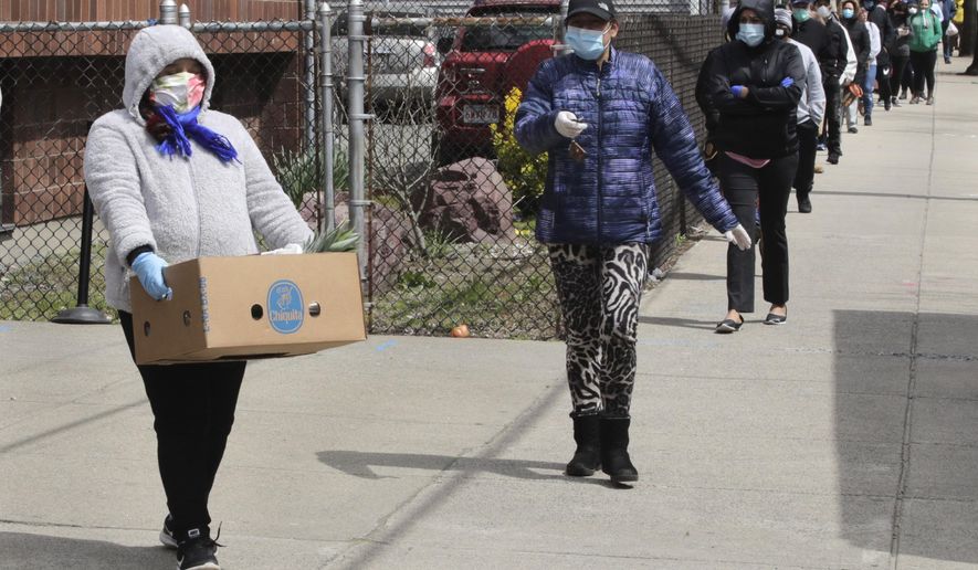 A woman carries a box of food away as hundreds others impacted by the COVID-19 virus outbreak wait in line at a Salvation Army center in Chelsea, Mass., Wednesday, April 22, 2020. (AP Photo/Charles Krupa)